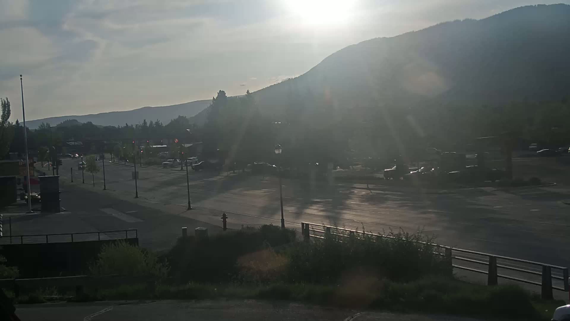 A sunny, hazy day reveals a street scene with parked cars, a roadway, and a mountain backdrop.