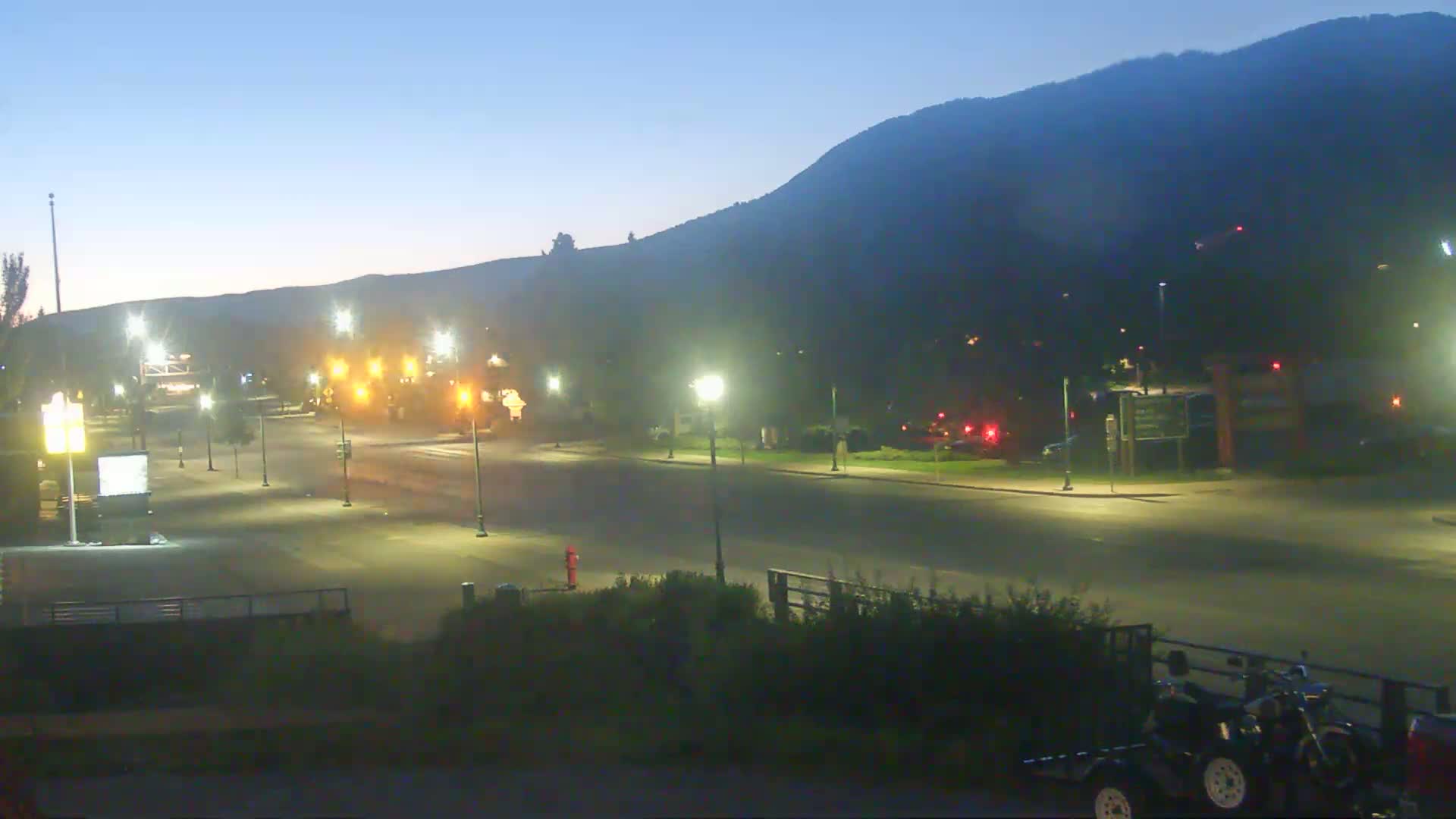 A mostly empty, well-lit street at twilight, with a large hill in the background.