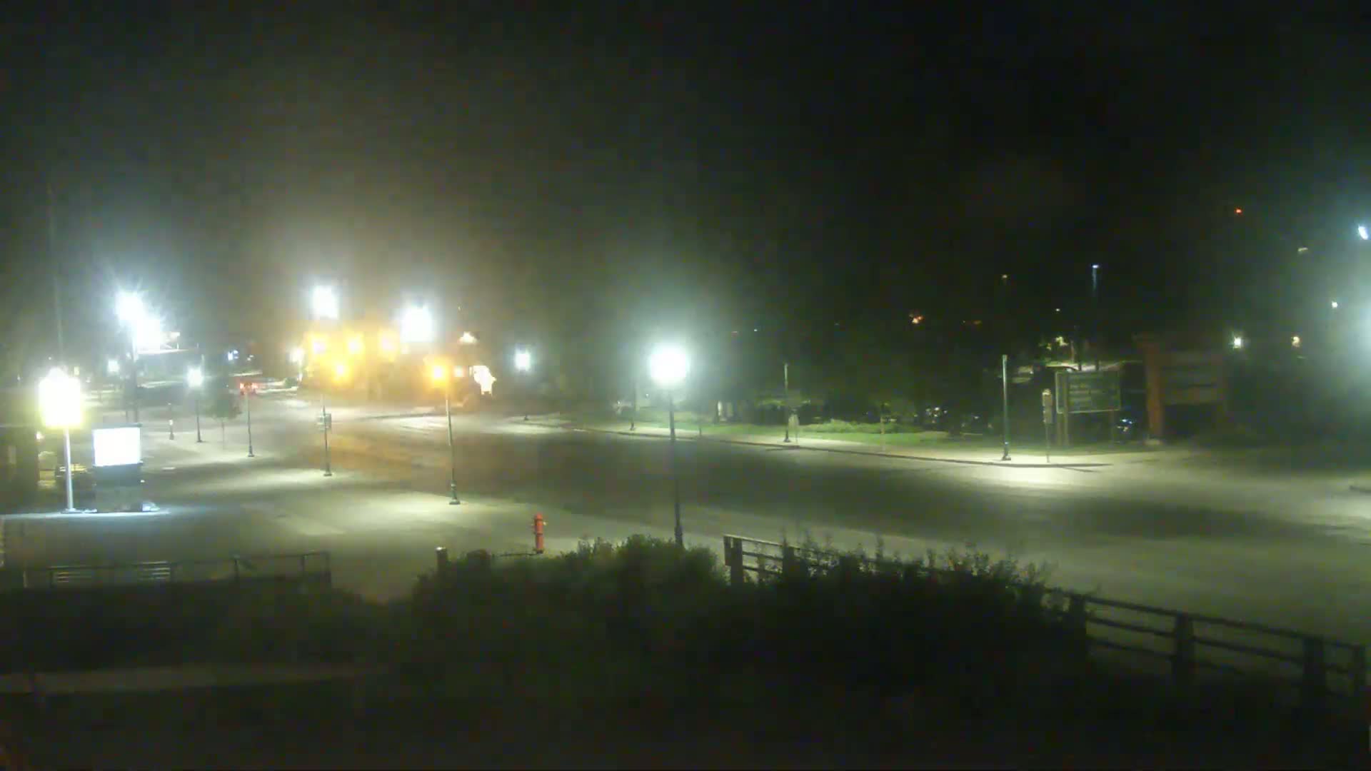 A nighttime, hazy view of a mostly empty roadway with streetlights illuminating the scene.