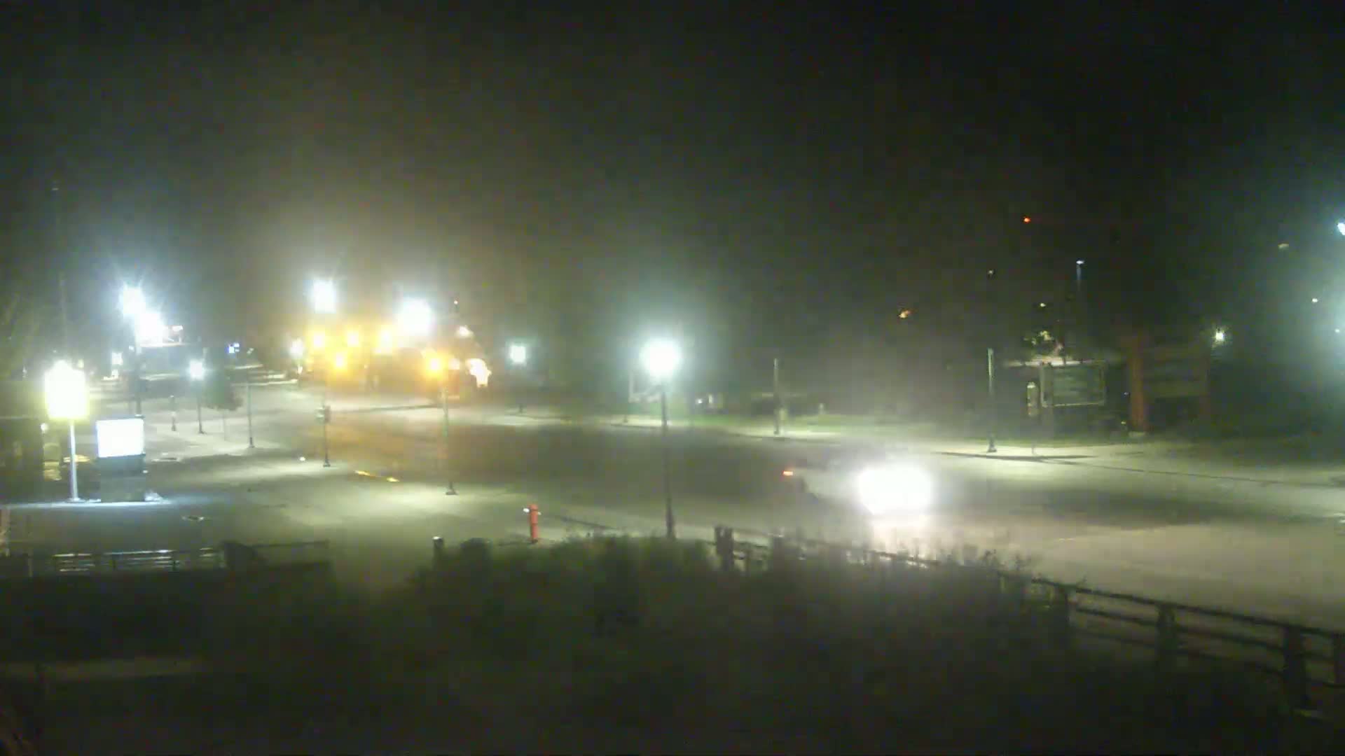 A hazy night scene shows a dimly lit intersection with a few vehicles and streetlights.