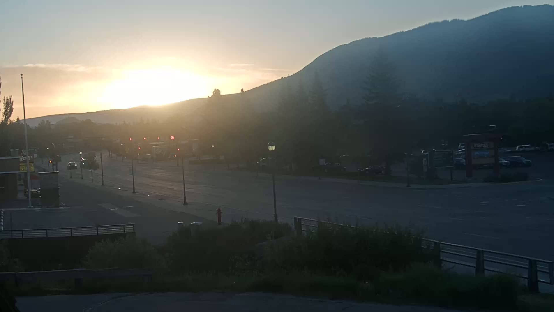 A hazy sunrise illuminates a quiet street scene with a mountain in the background.