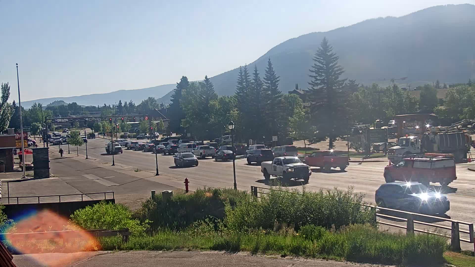A line of cars sits at a traffic light on a sunny day in front of a mountain range.