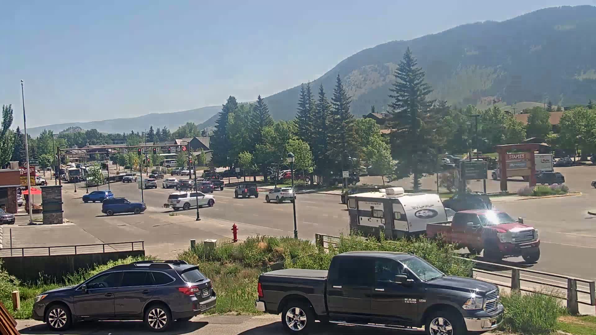 A sunny day reveals a mountain range in the background, with a busy intersection of cars and trucks in the foreground, including a camper and several pickup trucks.