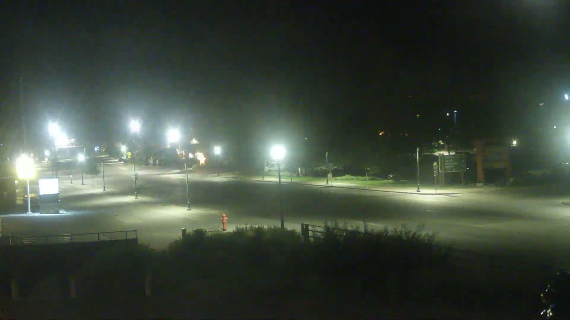 A mostly empty, well-lit roadway at night is visible, with some vegetation and streetlights along the sides.