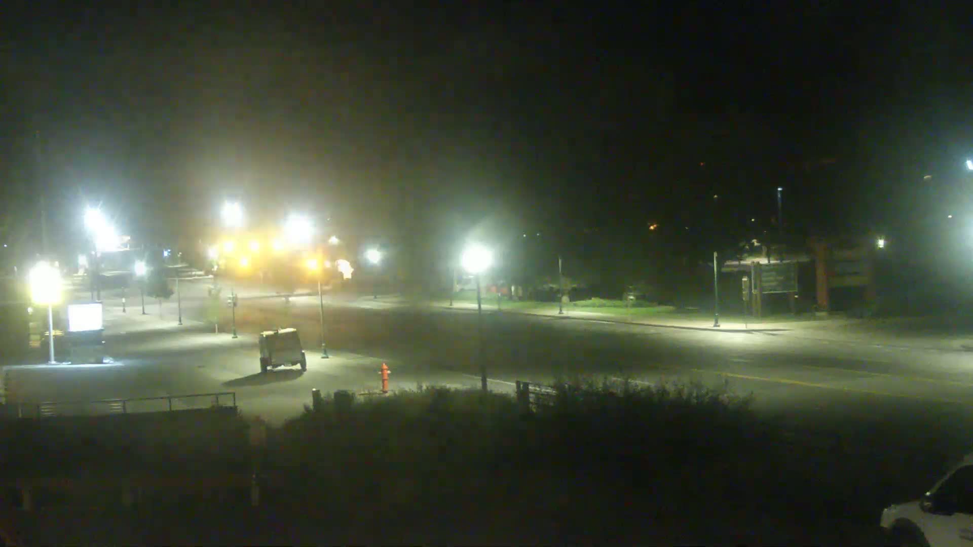 A mostly empty, dimly lit road at night is seen under hazy conditions, with a few vehicles and streetlights visible.