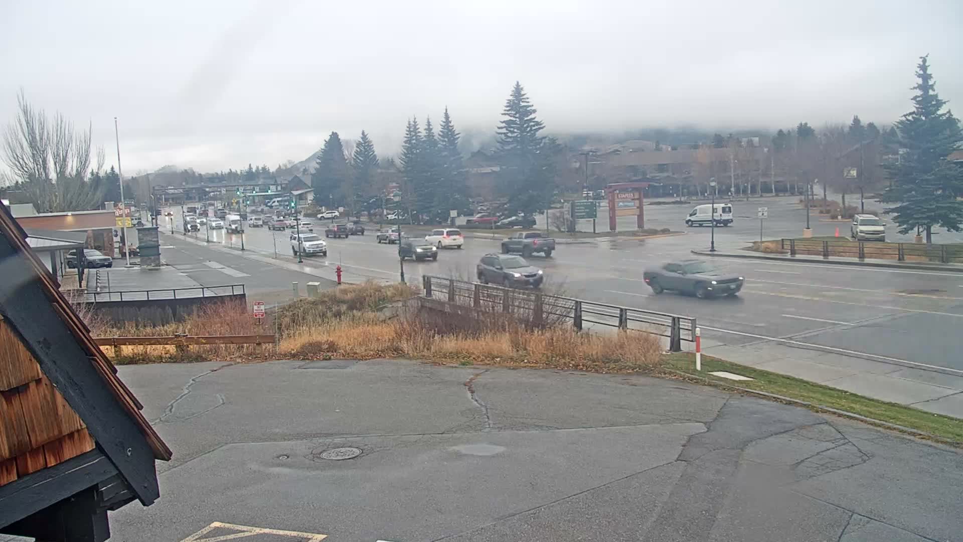 A hazy, rainy night view captures a wet outdoor urban area with numerous bright streetlights and building lights reflecting on the dark, water-slicked surfaces.
