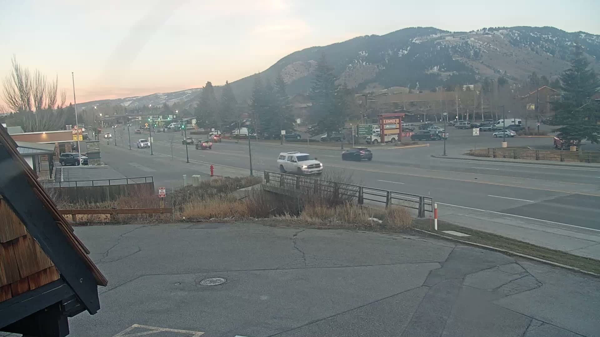 An empty, snow-covered outdoor area is brightly illuminated at night by numerous streetlights and festive holiday decorations on buildings and a large Christmas tree, under an overcast sky.