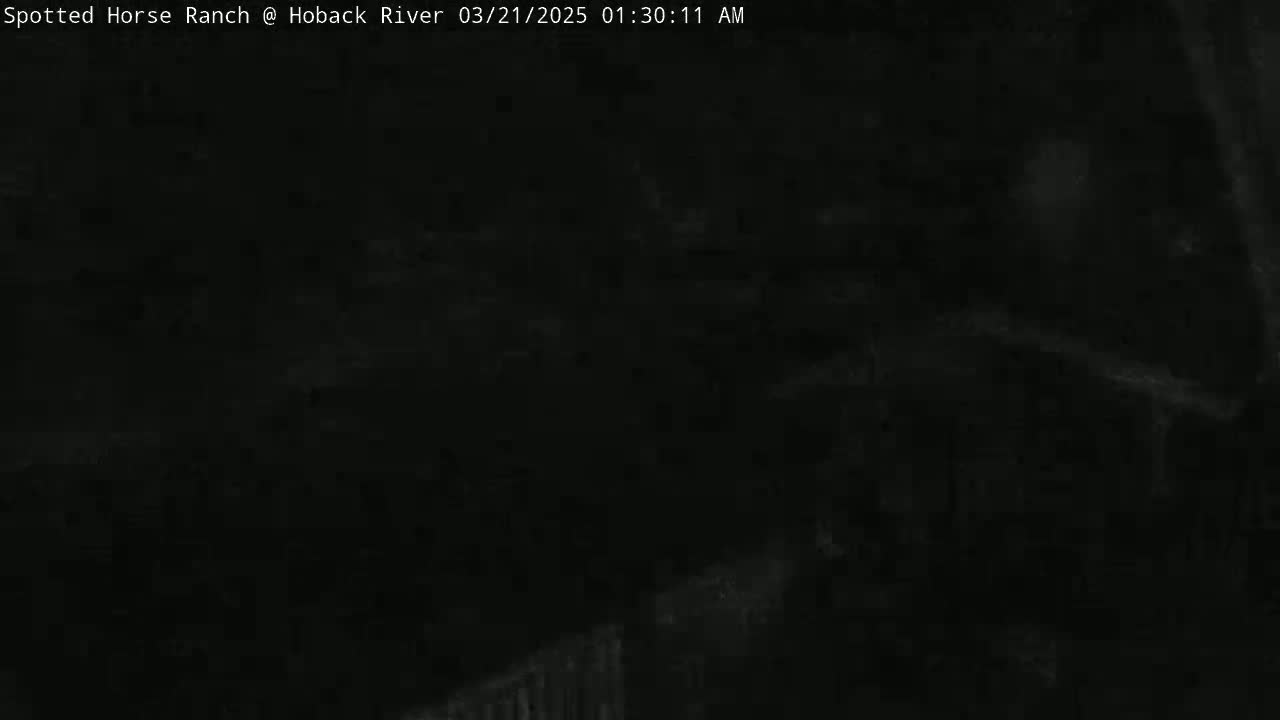 A very dark, nighttime image shows a mostly indiscernible scene with faint, blurry shapes suggesting an outdoor setting.