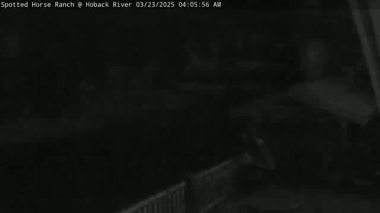 A dark, nighttime image shows a portion of a fence or railing in the lower right corner, with an indistinct, dark background.