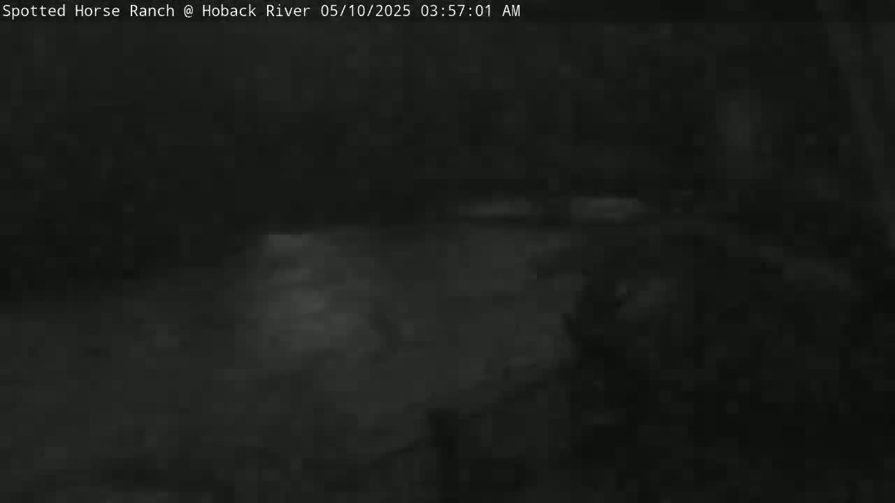 A dark, nighttime outdoor scene shows a blurry, indistinct area with a possible body of water, under cloudy conditions.