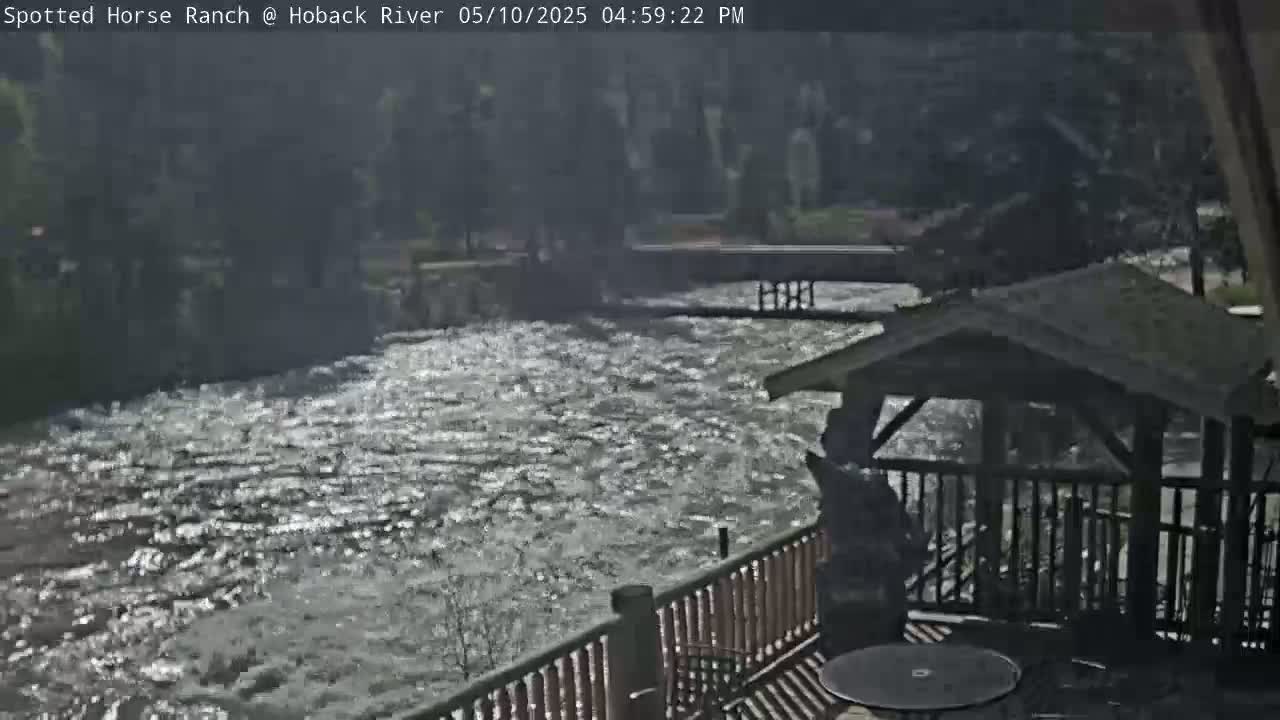 A swiftly flowing river is viewed from a deck with a gazebo on a sunny day.