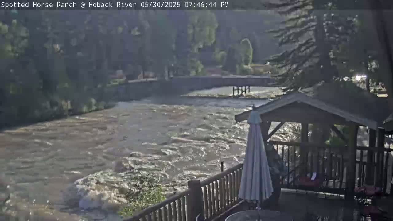 A fast-flowing river is seen from a deck with a gazebo, under a partly sunny sky.