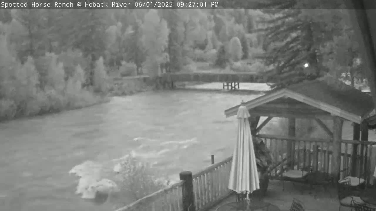 A swiftly flowing river is seen from a deck with a gazebo and umbrella, under an overcast sky.