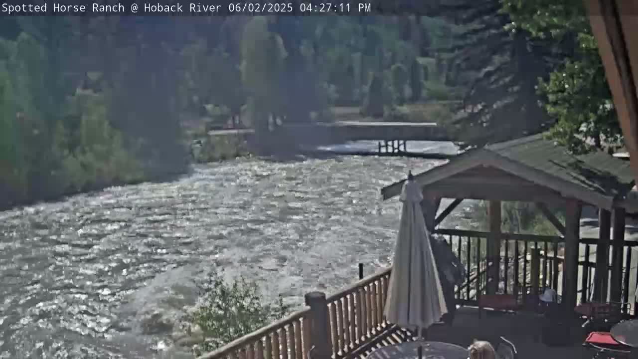 A fast-flowing river is seen from a deck with a gazebo, under a sunny sky.
