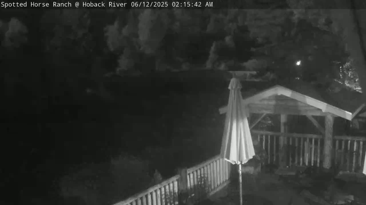 A nighttime, cloudy scene shows a partially covered patio with a white umbrella, railing, and gazebo.