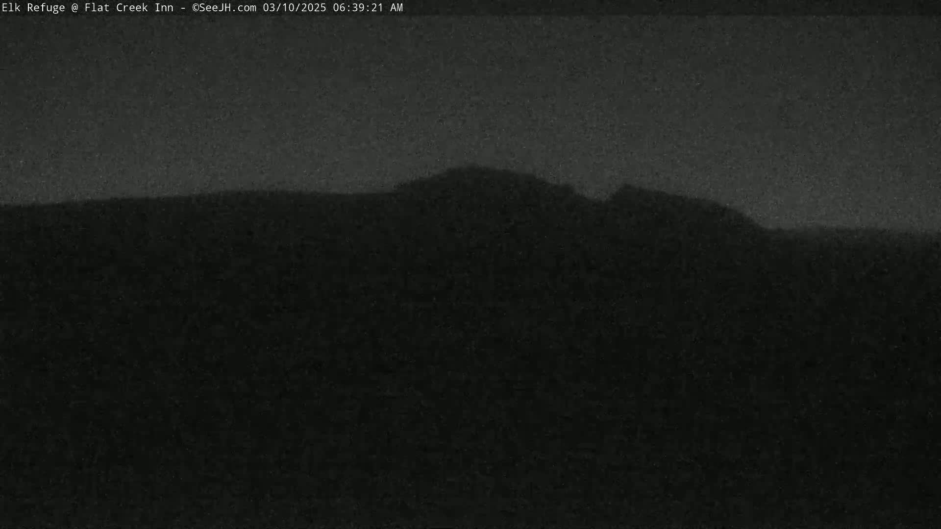 A dark, nighttime outdoor scene shows a silhouetted mountain range against a mostly clear sky.