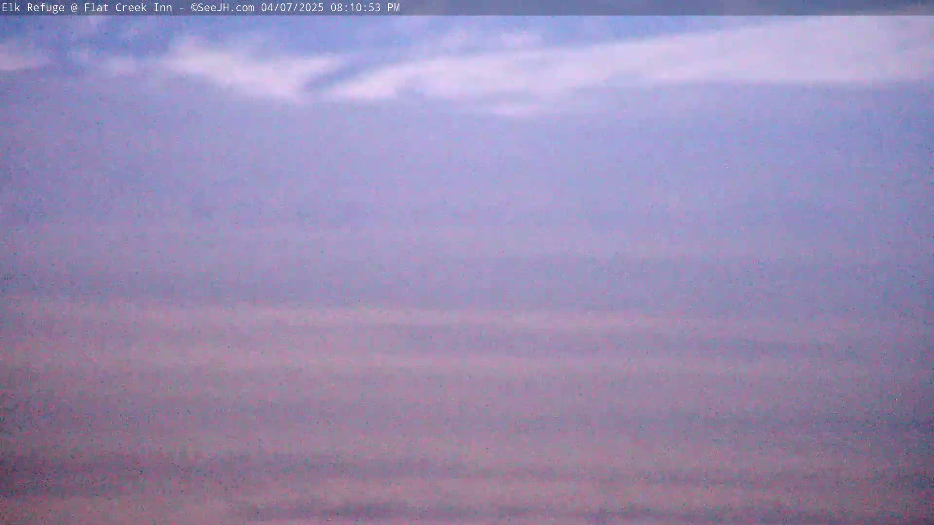 A hazy, pale purple and pink landscape stretches to the horizon under a mostly cloudy sky.