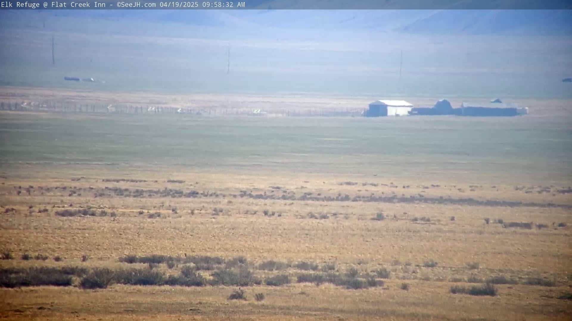 A hazy, flat, dry landscape stretches to the horizon, featuring a cluster of buildings in the mid-ground.