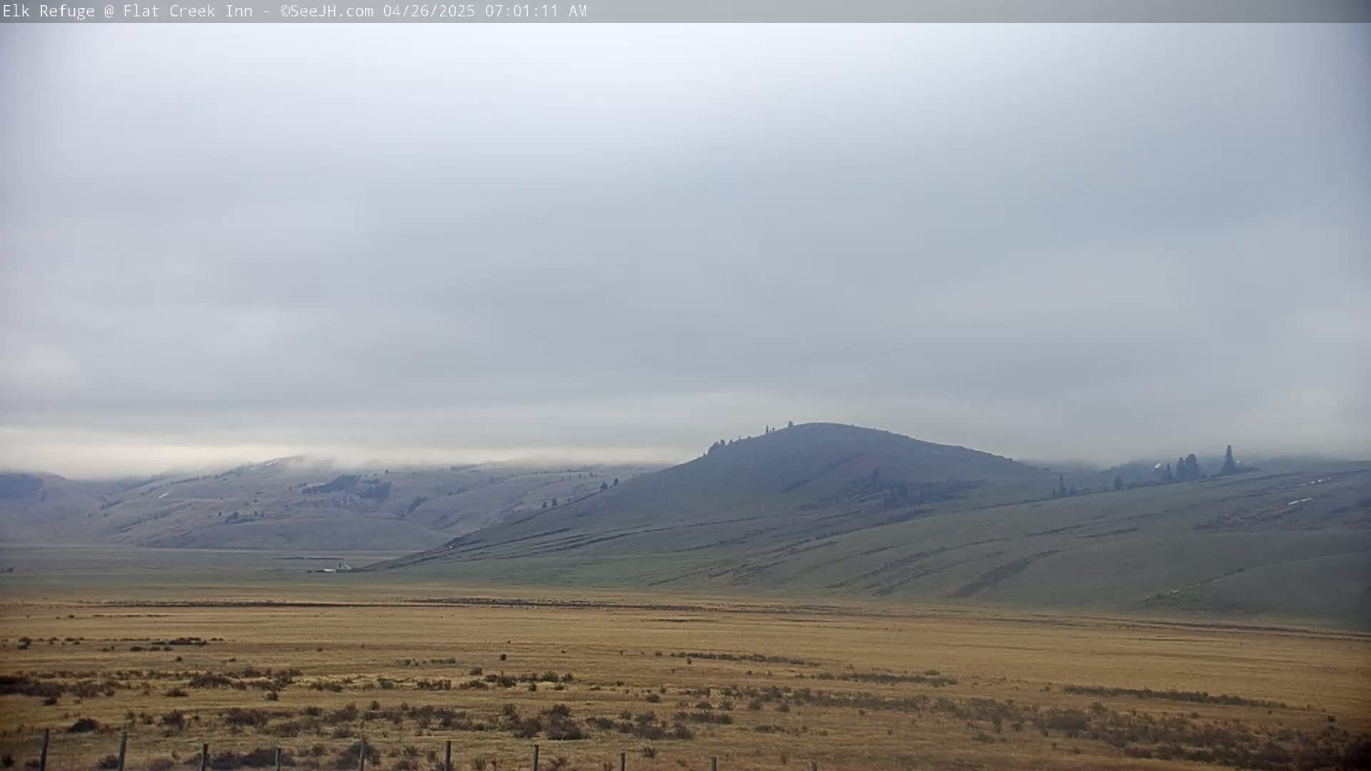 A flat, tan plain stretches to rolling, green hills under a hazy, overcast sky.