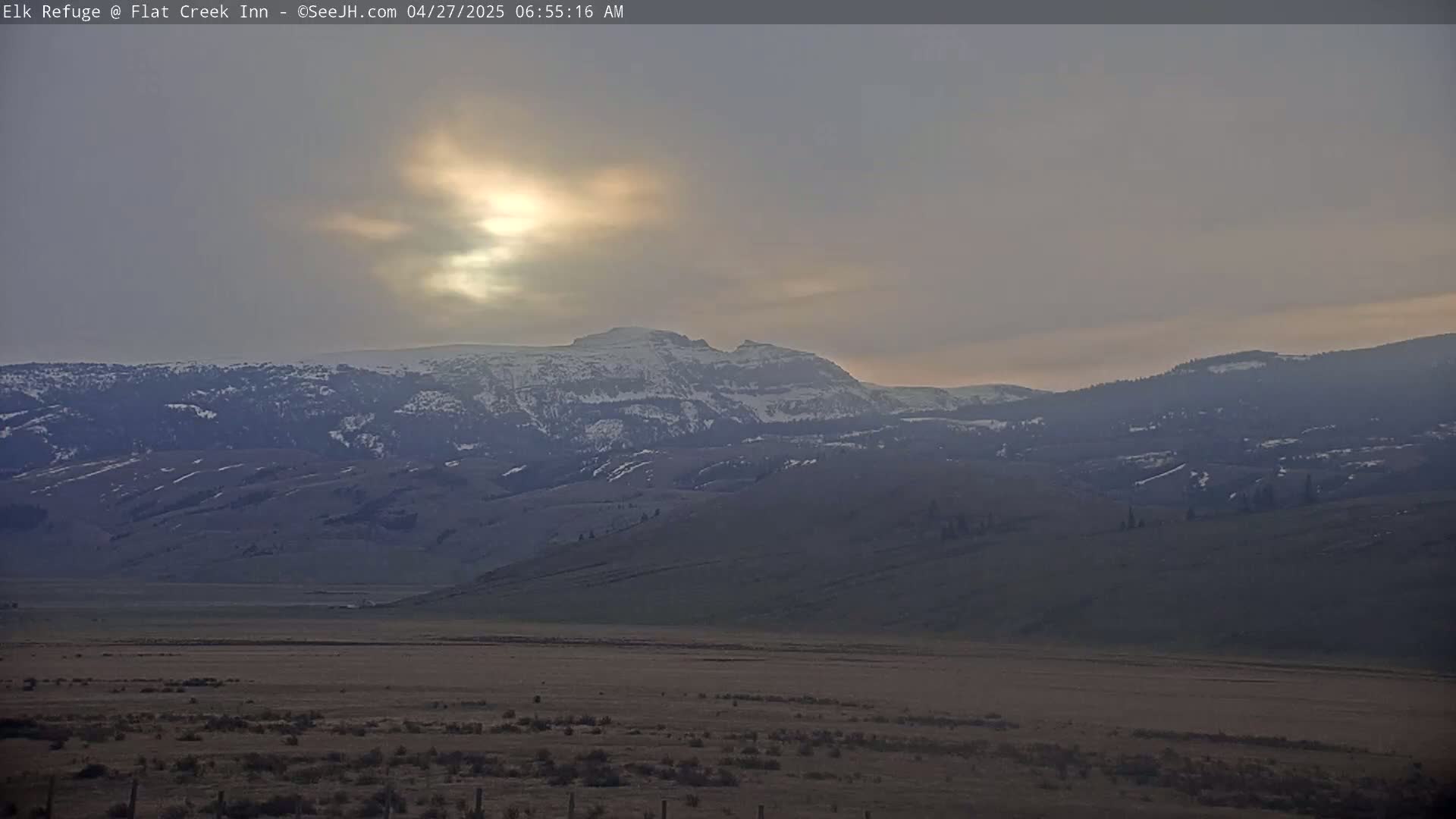 A hazy sunrise illuminates snow-capped mountains and a vast, flat valley.