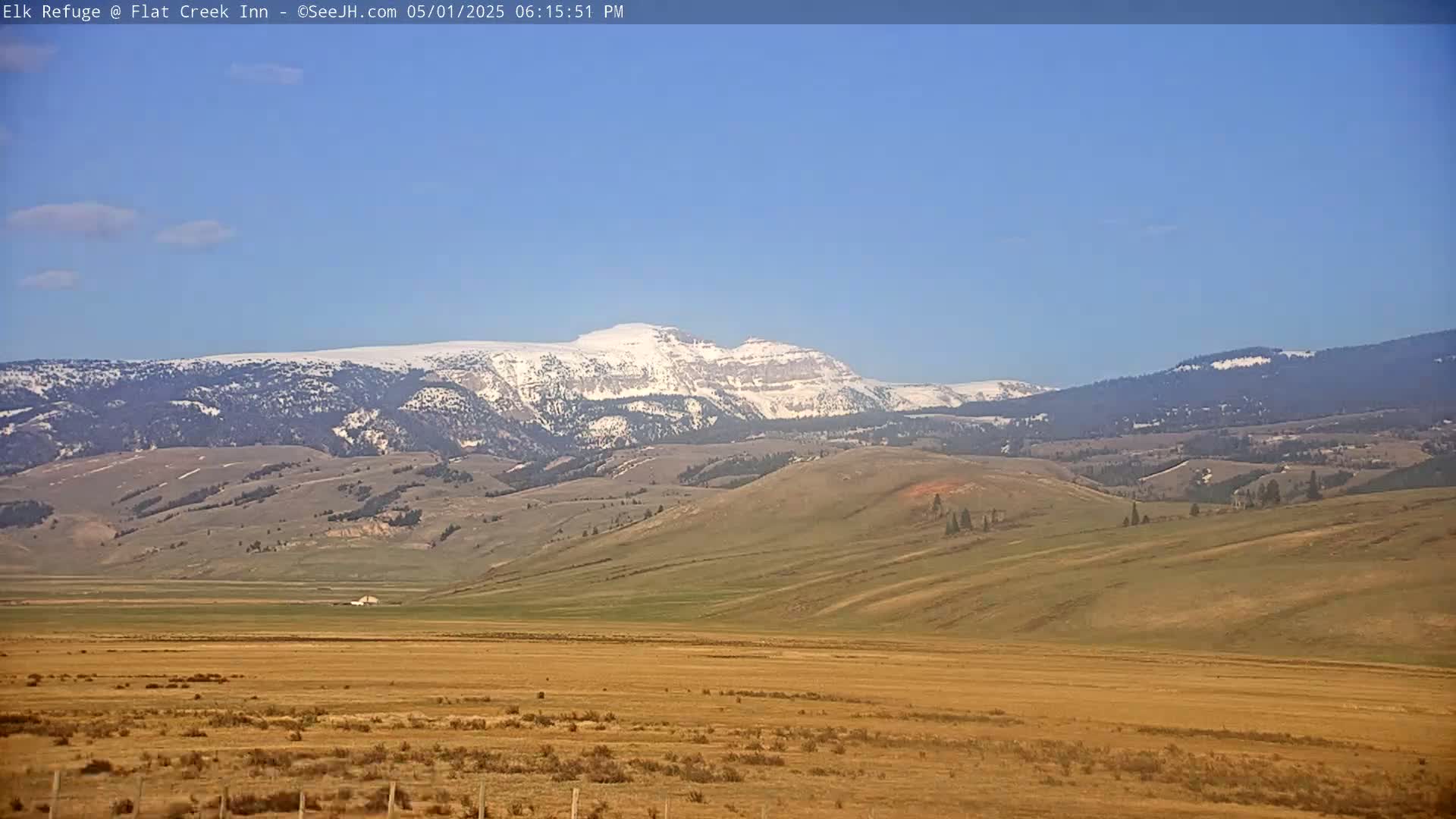 A snow-capped mountain range is visible in the distance above a vast, flat, dry landscape under a clear blue sky.
