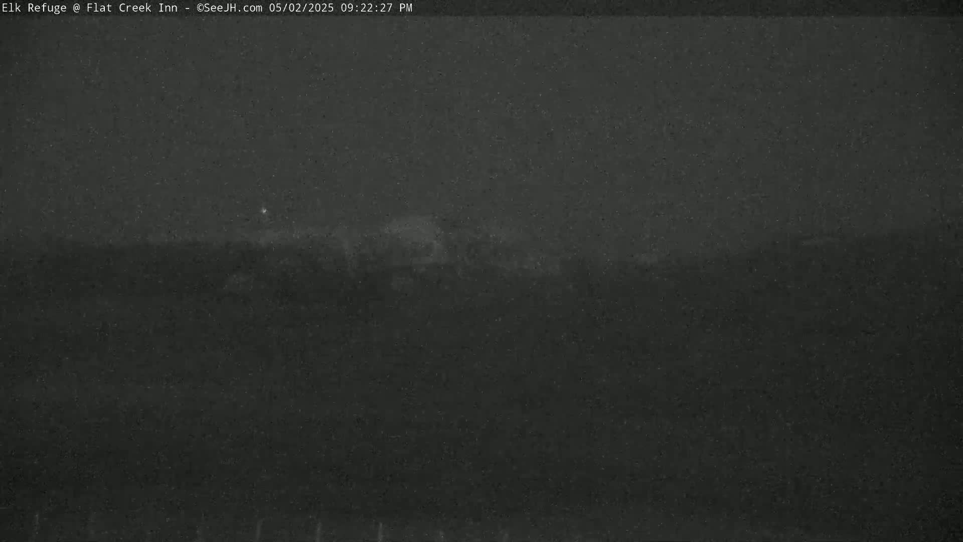 A dark, nighttime landscape is visible under a mostly clear sky, with a faint light source in the distance.