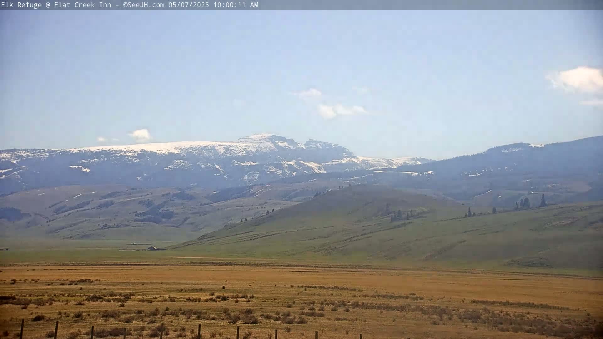 A snow-capped mountain range is visible in the distance under a clear, light blue sky, overlooking a vast expanse of tan and green rolling hills.