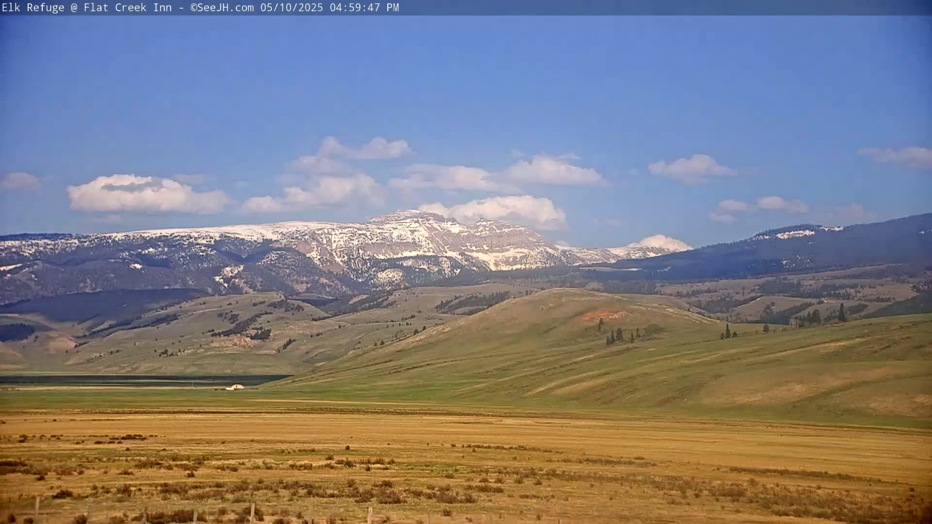 A snow-capped mountain range is visible in the distance under a mostly clear blue sky, with rolling hills and a flat plain in the foreground.