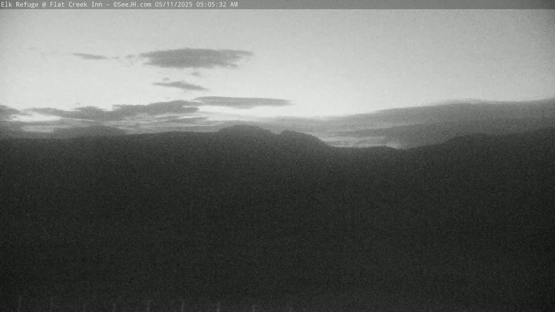 A grayscale image shows a pre-dawn sky with thin clouds over dark mountains.