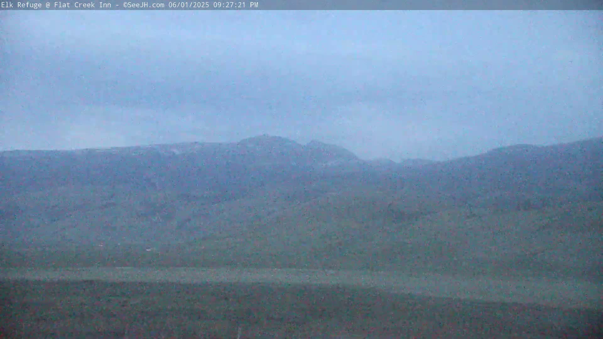 A hazy, overcast sky hangs over a muted landscape of rolling hills and distant mountains.