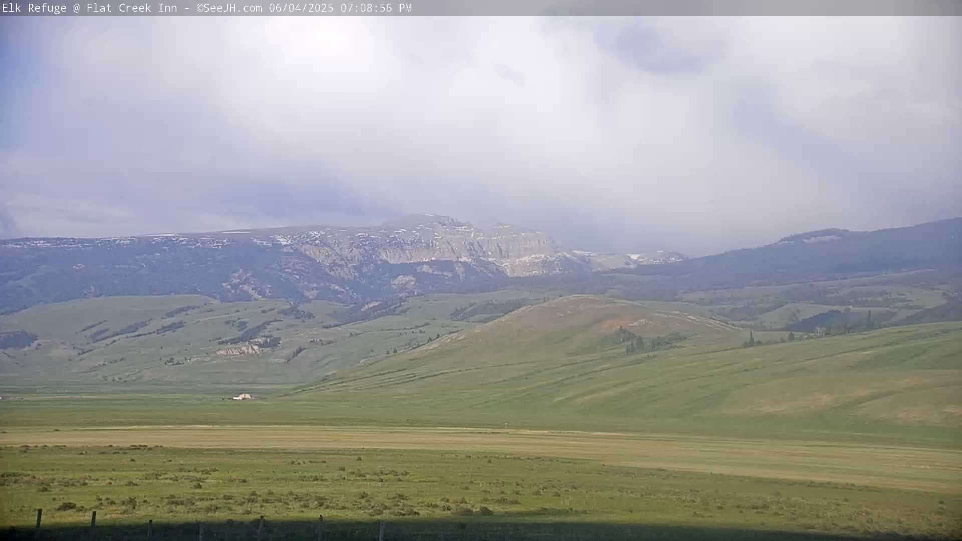 A vast, rolling green landscape stretches to distant mountains under a partly cloudy sky.