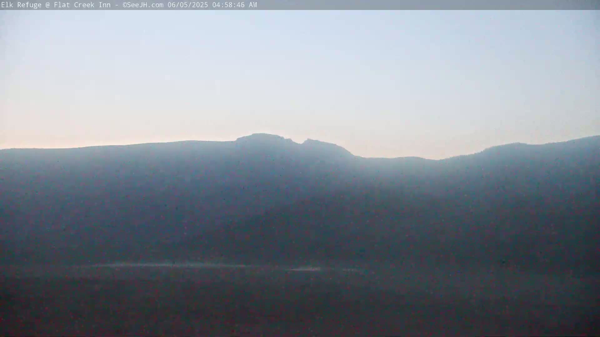 A hazy, light-blue sky sits above a dark, mountainous landscape.
