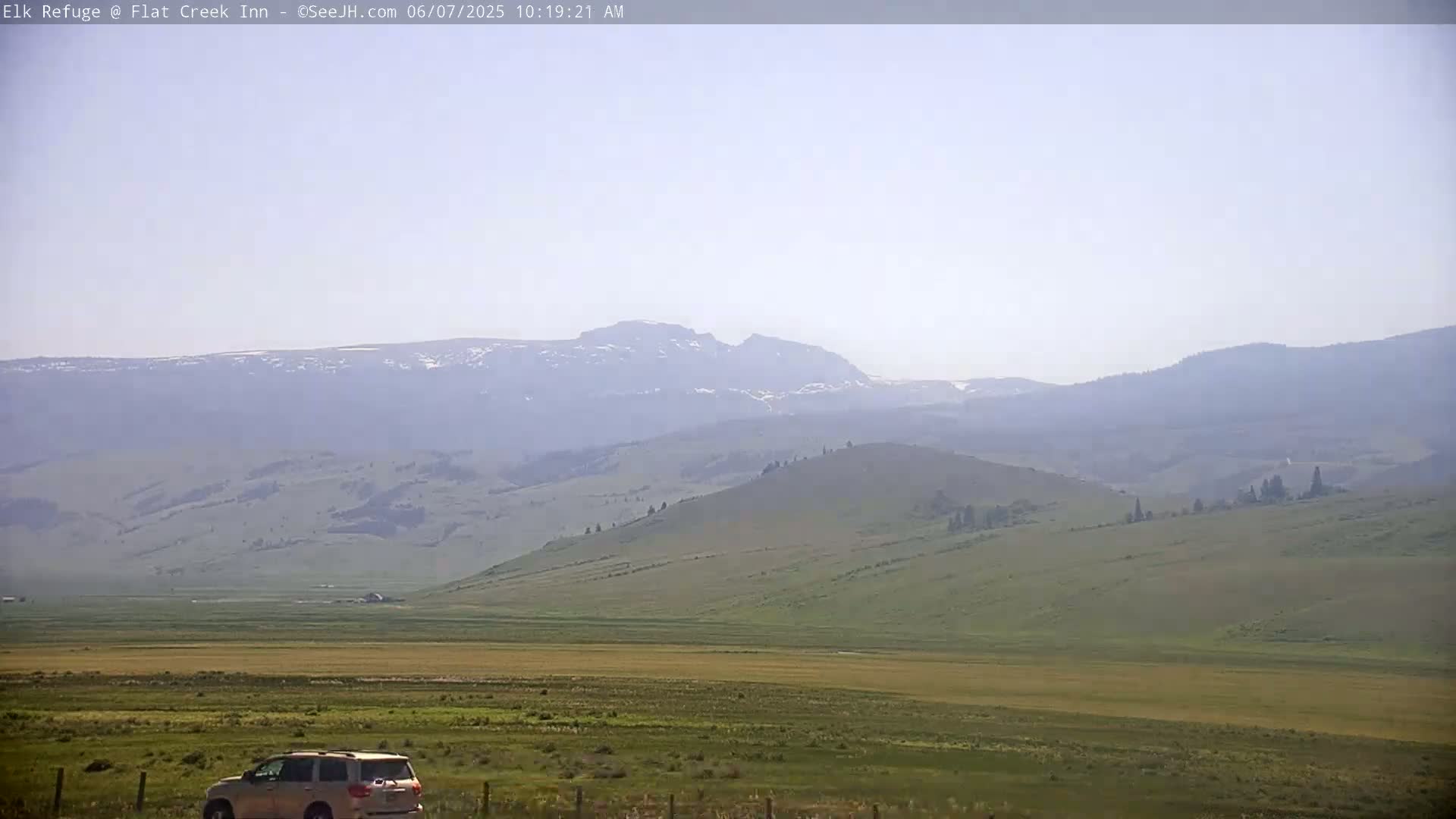 A hazy view shows a tan and green rolling landscape with distant mountains under a light-blue sky.