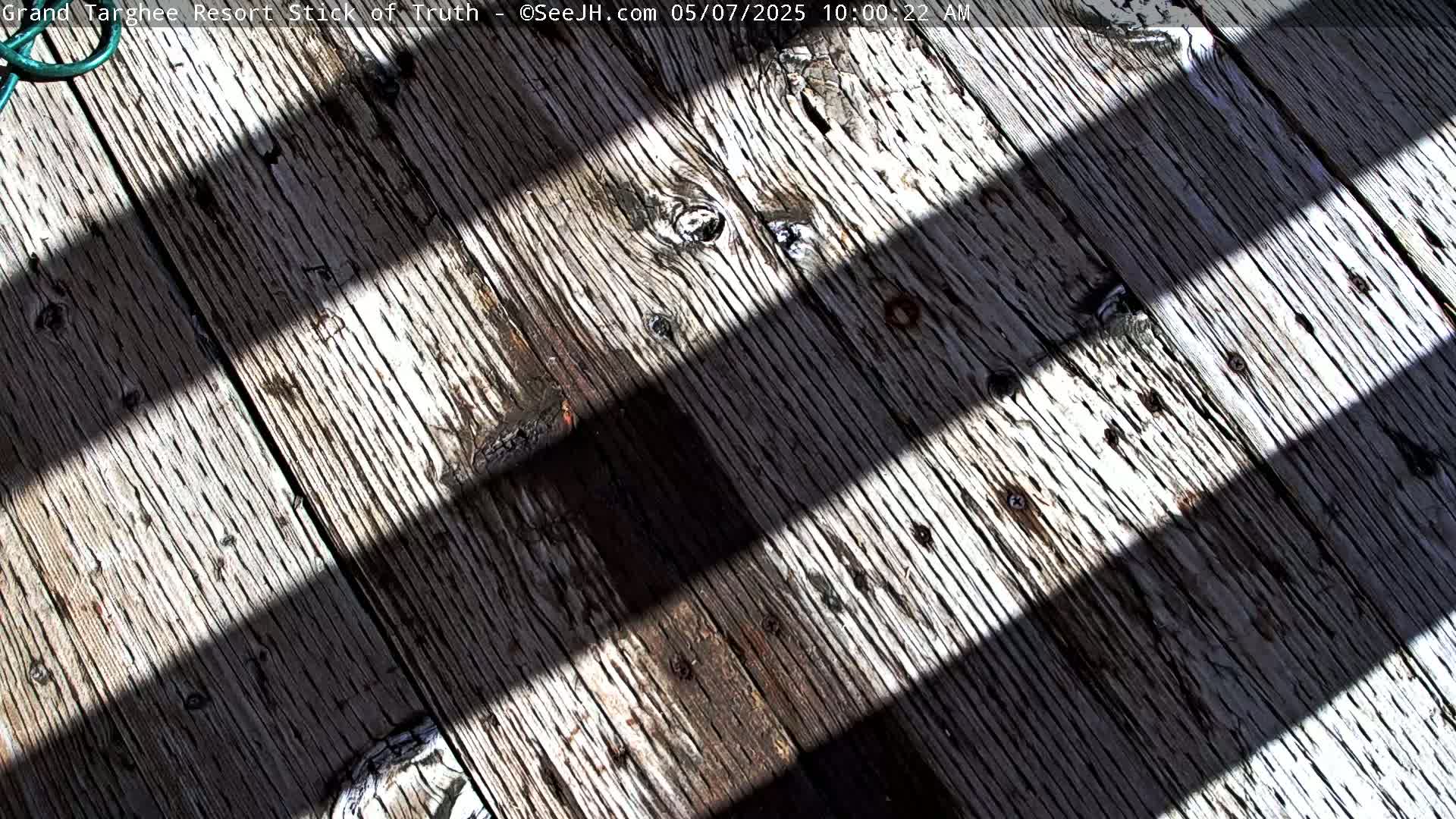 Weathered wooden planks are crisscrossed by parallel shadows in bright sunlight.