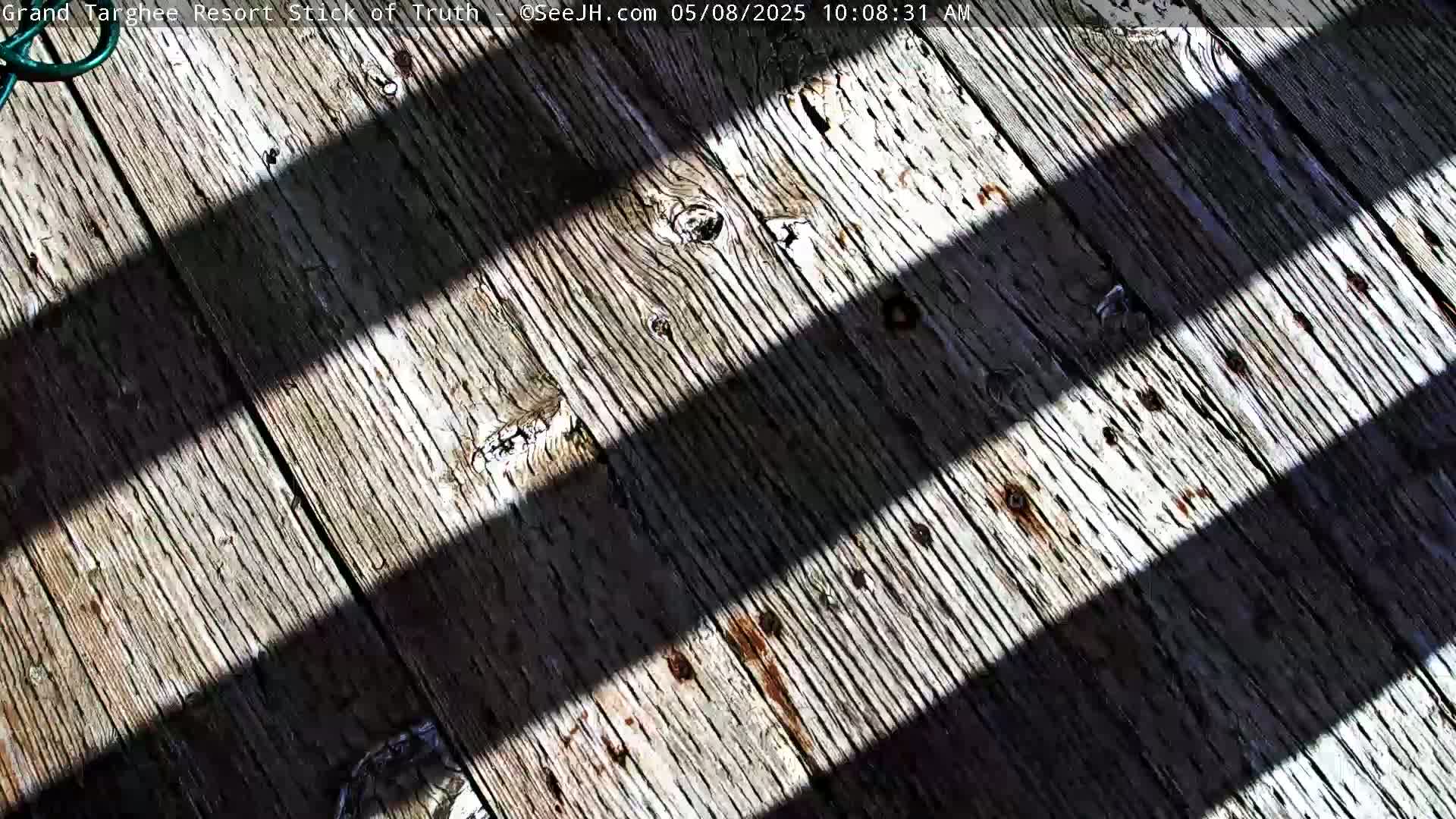 Two parallel shadows cross a weathered wooden surface outdoors in sunlight.