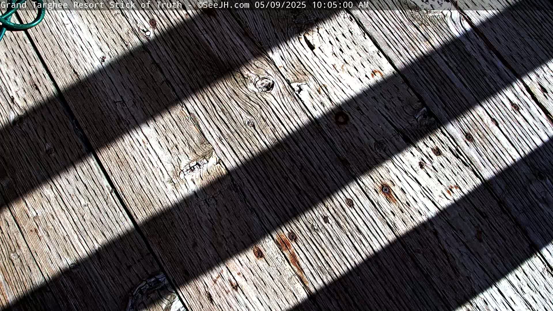 Two parallel diagonal shadows cross a weathered wooden surface in bright sunlight.