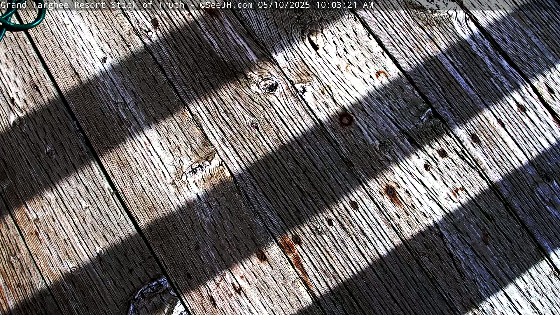 Three parallel shadows cross a weathered wooden deck in bright sunlight.