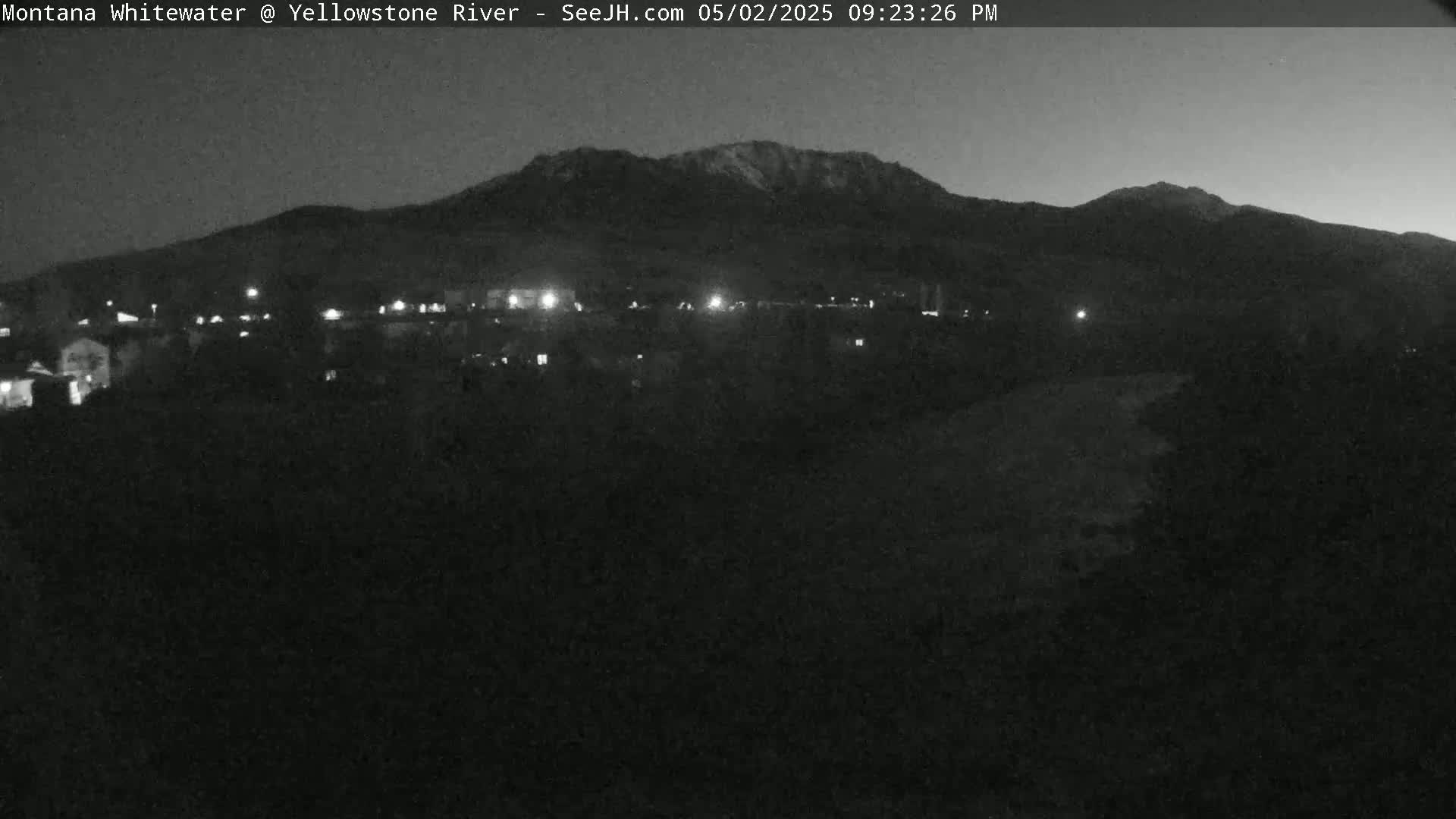 A nighttime, low-light view shows a mountain range in the distance behind a small town with scattered lights.