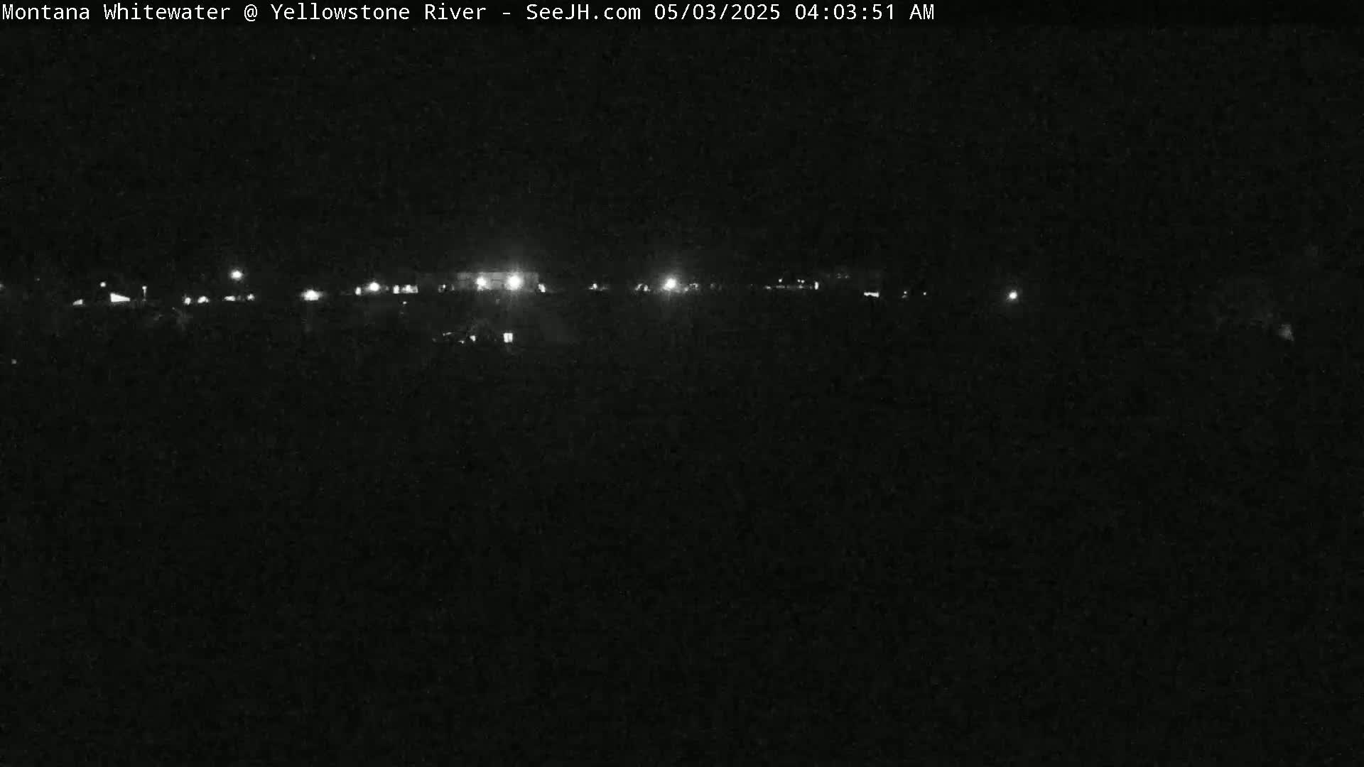 A nighttime, low-light view shows a distant line of lights, possibly from buildings or vehicles, under a dark sky.
