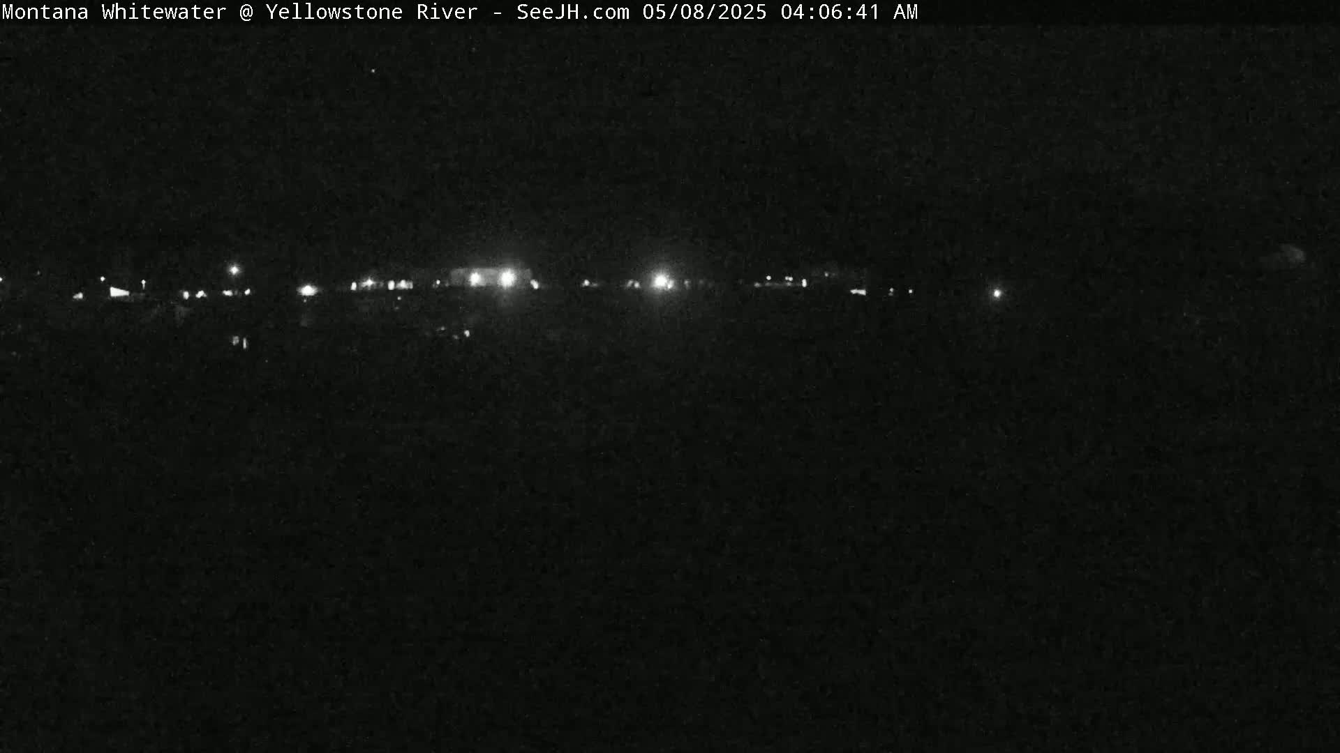 A nighttime, low-light view shows a dark landscape with a line of distant lights.