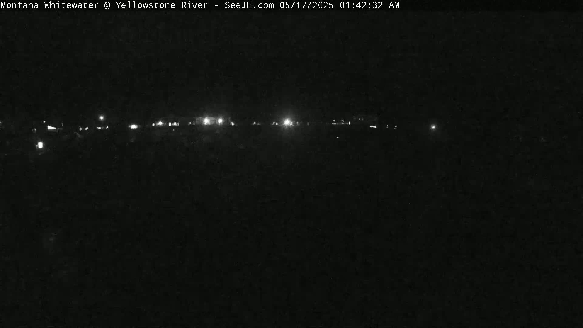 A nighttime, low-light view shows a dark landscape with a line of distant lights.