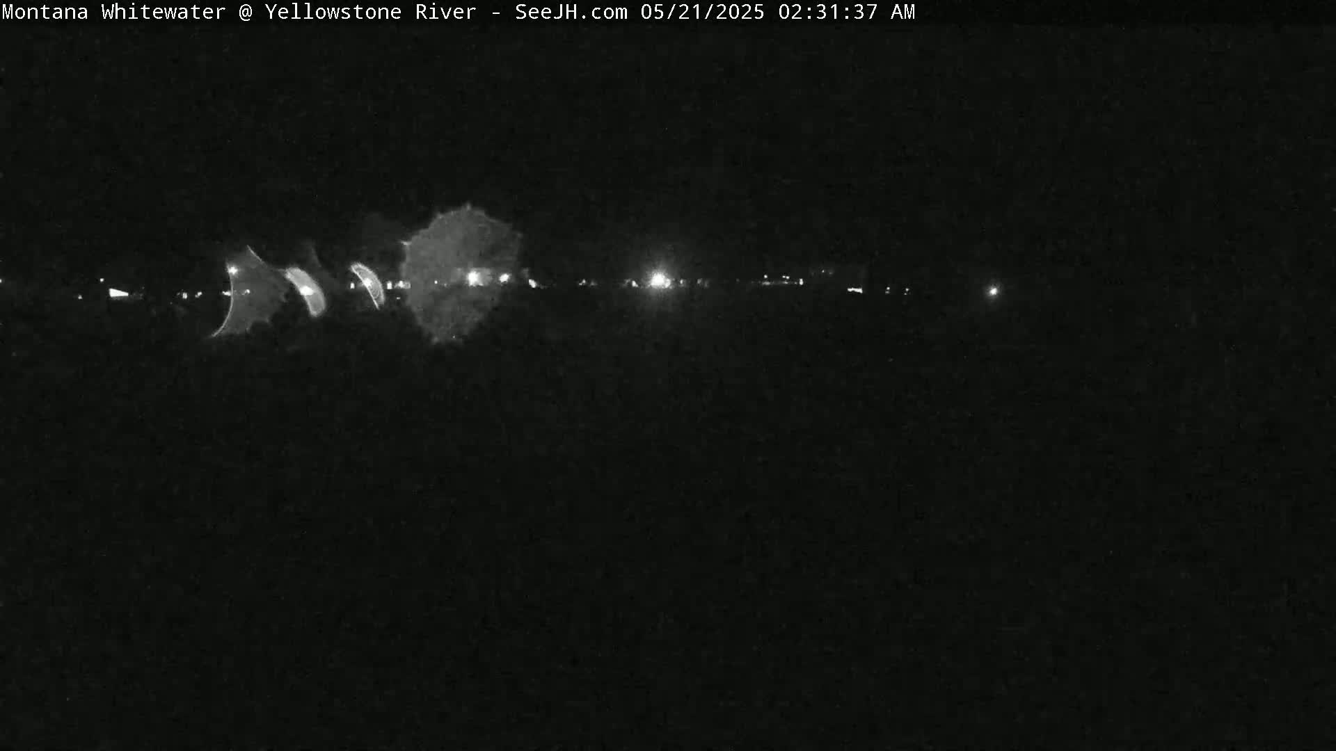 A nighttime, low-light image shows a dark landscape with a line of faint lights in the distance.