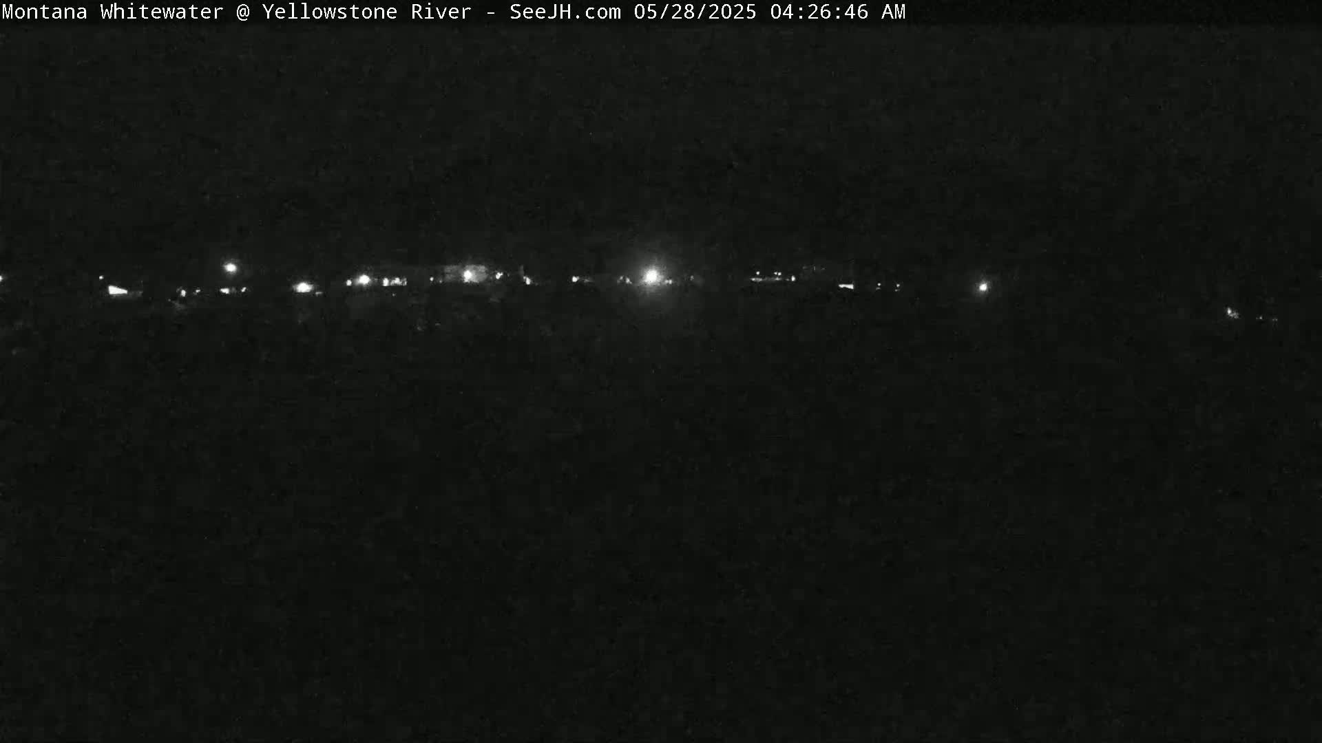 A nighttime, low-light view shows a distant line of lights across a dark landscape.