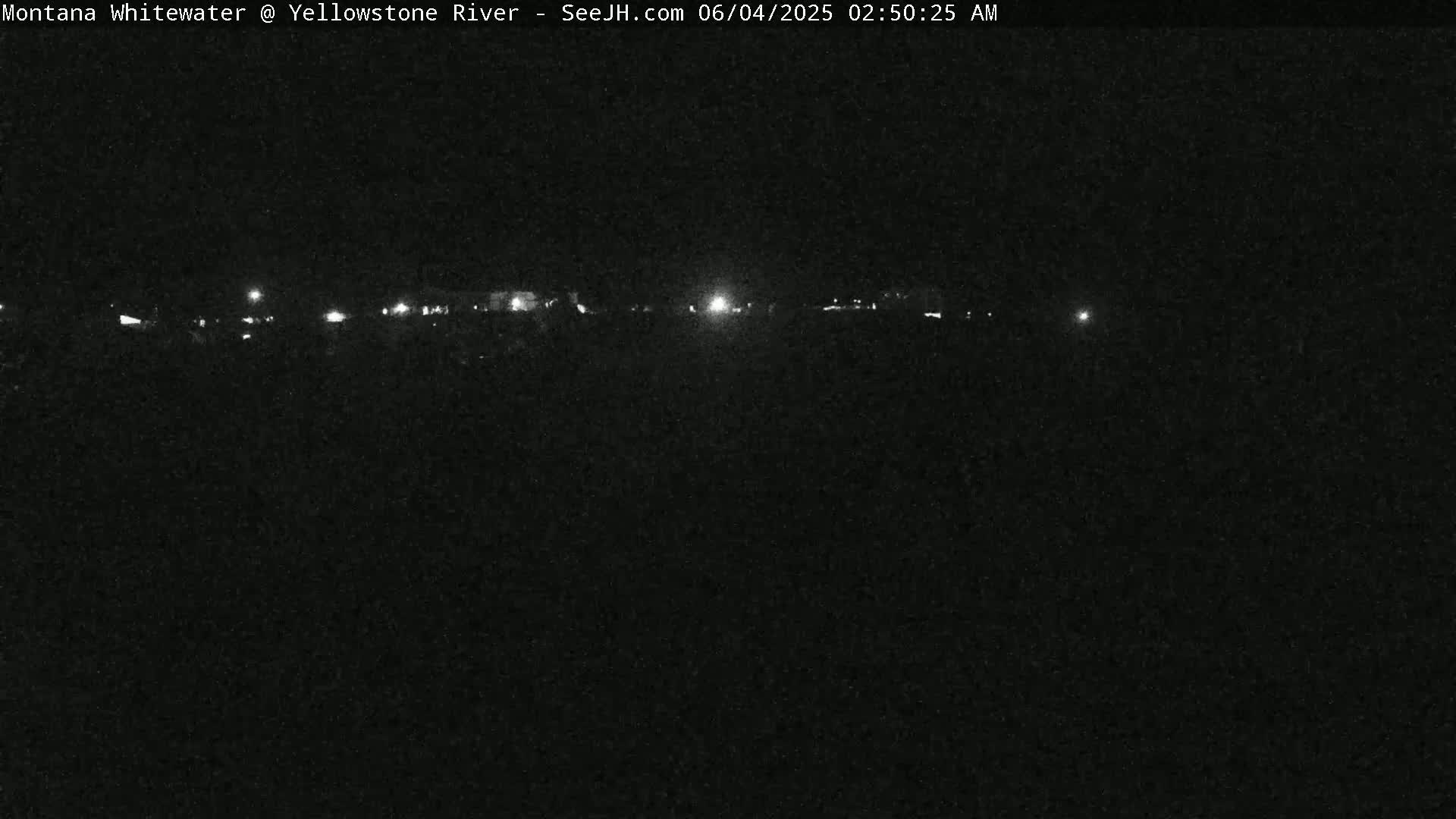 A nighttime, low-light view of a dark landscape with a line of faint lights in the distance.