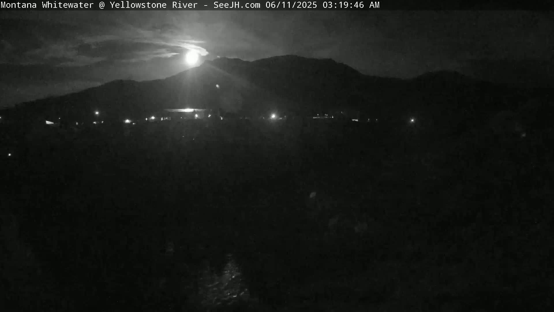 A nighttime, low-light view of a dark landscape with mountains in the background, illuminated by a bright moon or other light source.