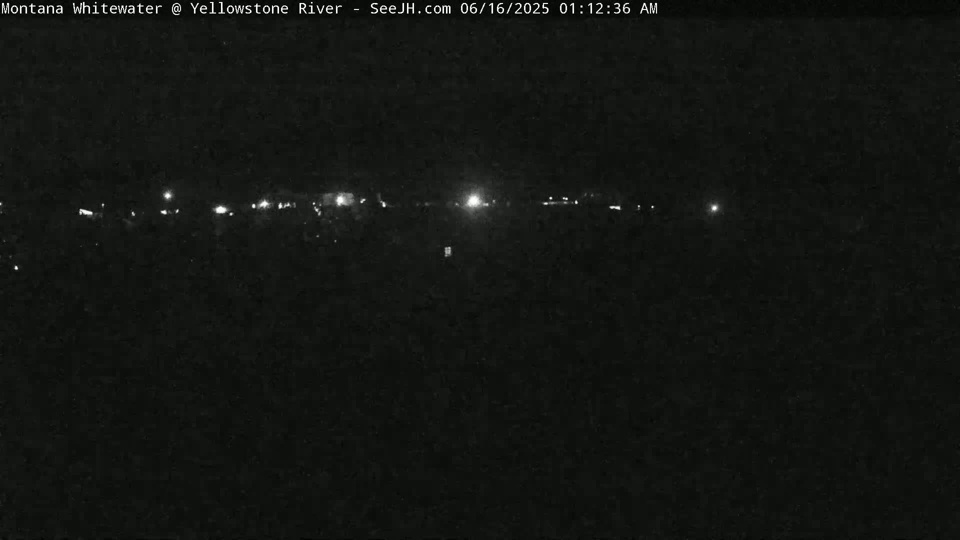 A nighttime long shot of a dimly lit landscape with a line of lights in the distance.