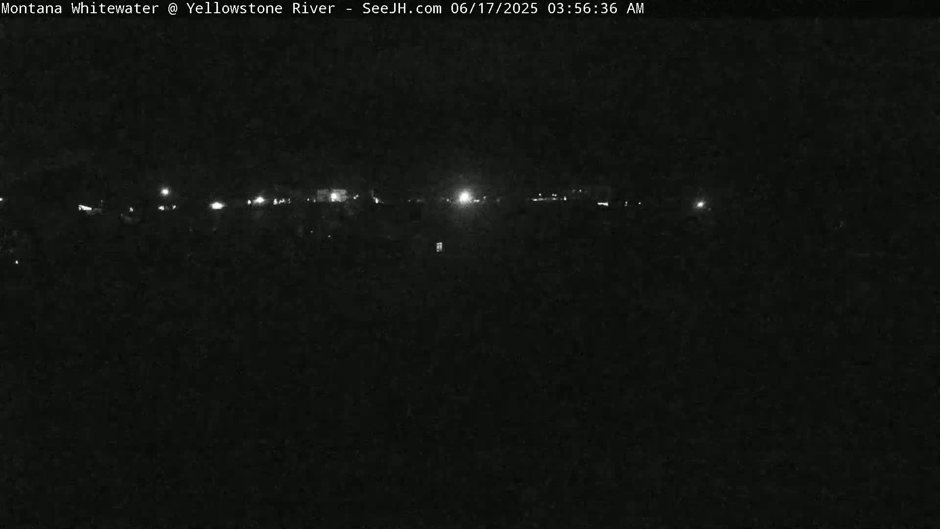 A nighttime, low-light view of a dark landscape with a line of distant lights.