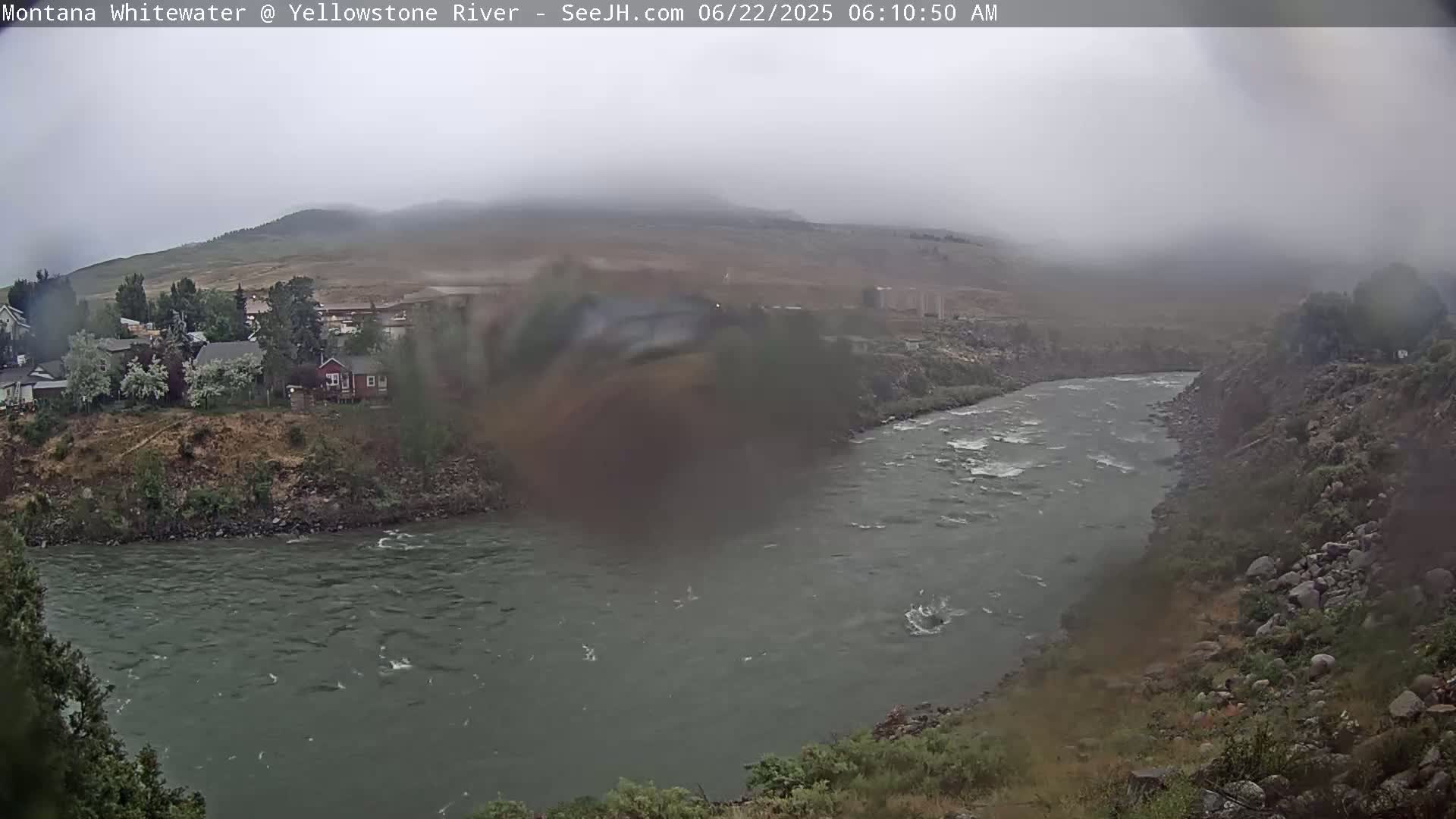 A river flows through a rocky landscape on an overcast day, with a small town visible in the distance.