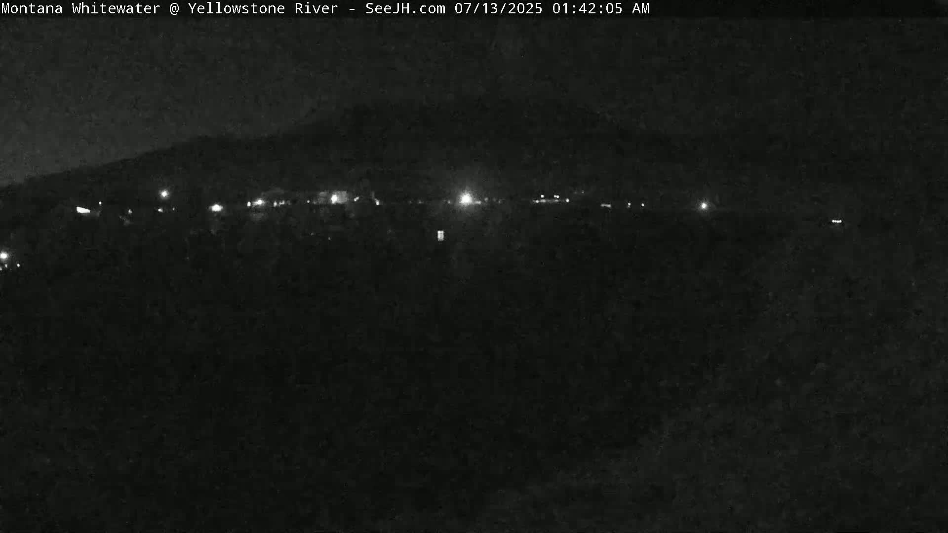 A nighttime, low-light view shows a dark landscape with a few scattered lights in the distance.