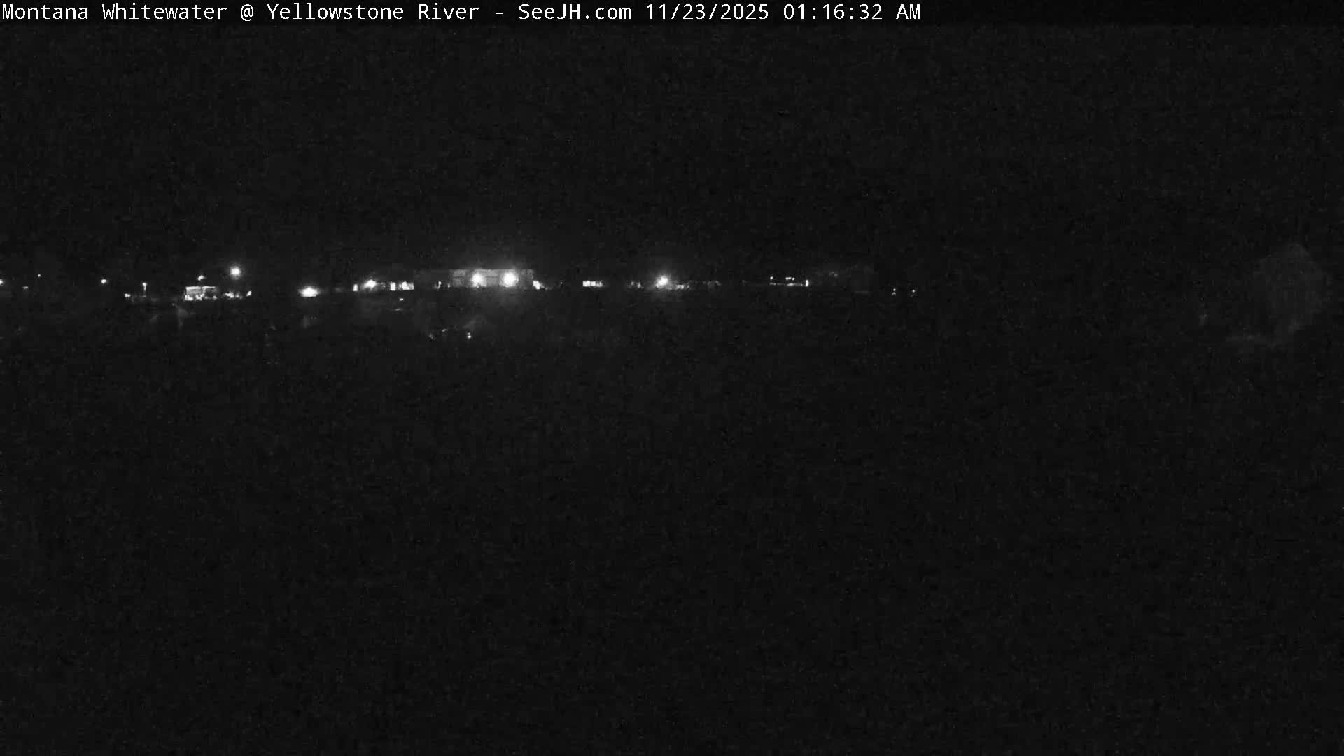 A very dark outdoor nighttime scene reveals a string of distant lights across the horizon under clear skies.